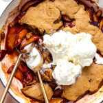 gluten free peach cobbler in a a quart baking dish topped with three scoops of vanilla icecream.