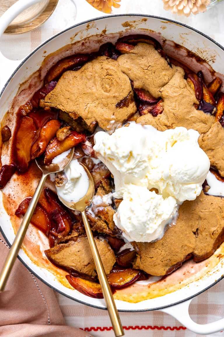 gluten free peach cobbler in a a quart baking dish topped with three scoops of vanilla icecream.