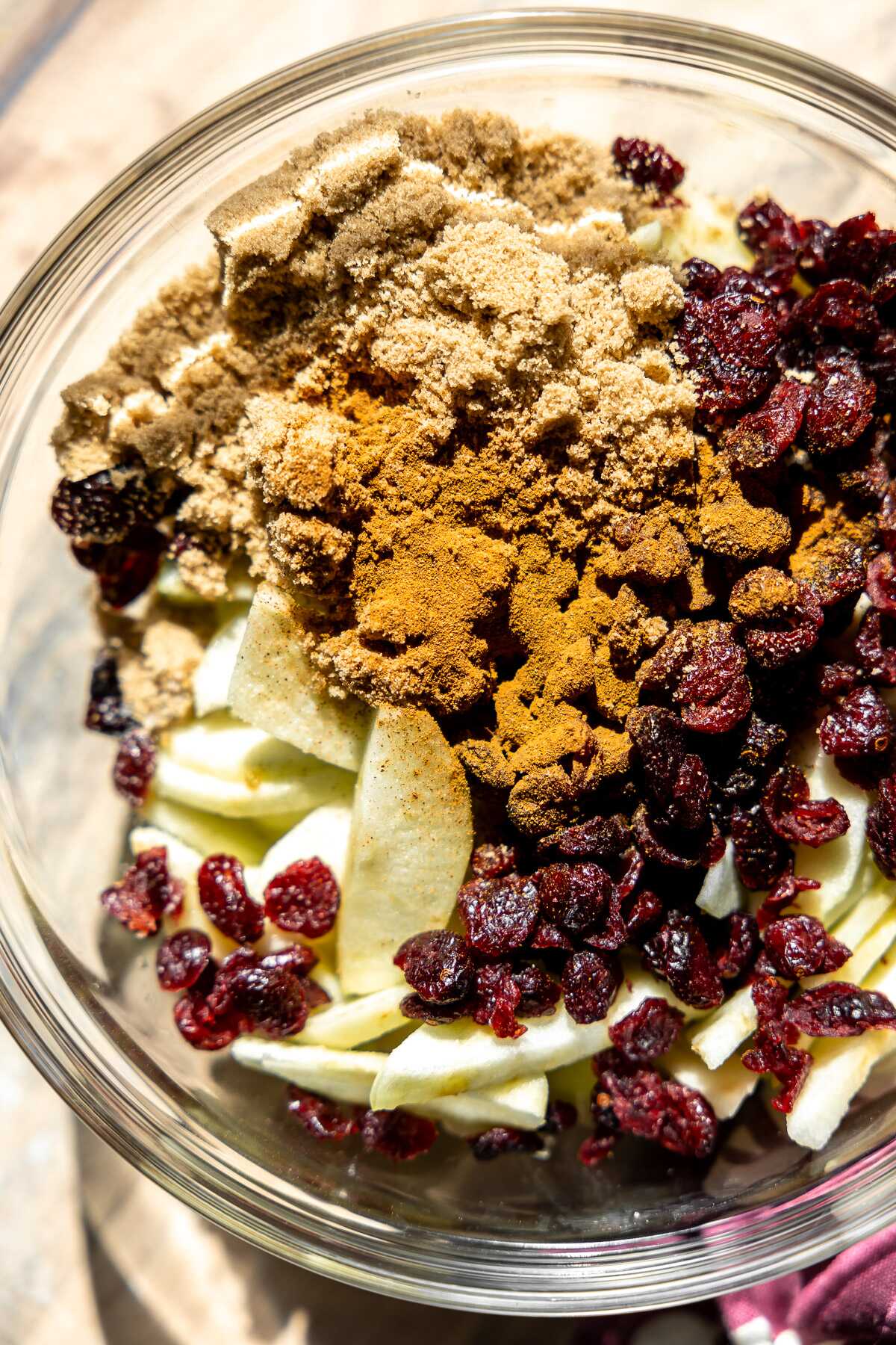 sliced apples, dried cranberries in a glass bowl sprinkled with brown sugar, cinnamon 