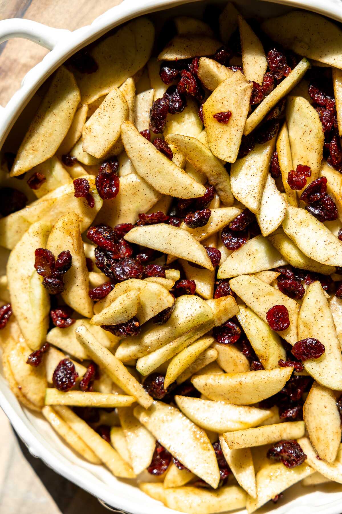 sliced apple and dried cranberries tossed in aeromatics and in a white dish. 