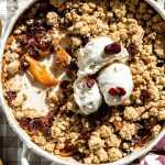 cranberry apple crumble in a dish with three scoops of vanilla ice cream scooped on top