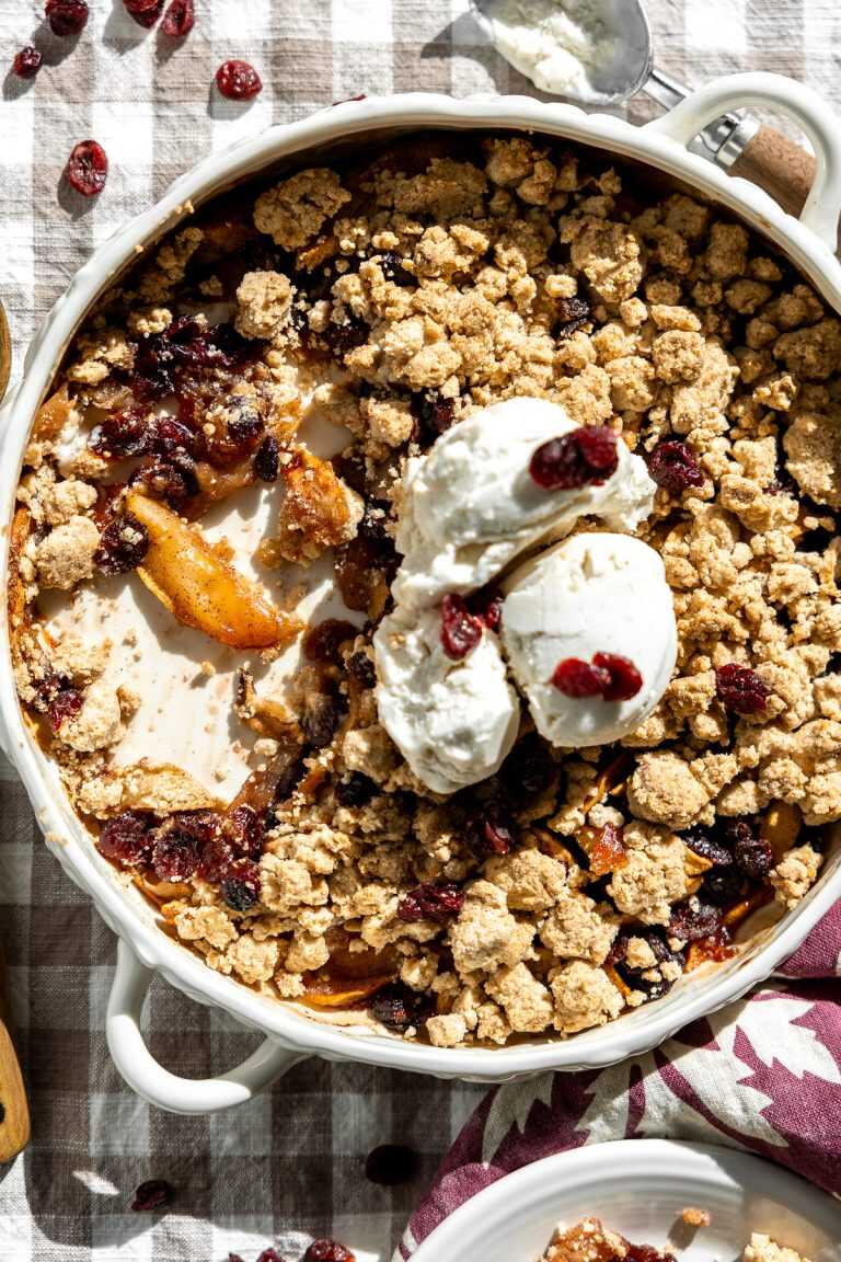 cranberry apple crumble in a dish with three scoops of vanilla ice cream scooped on top