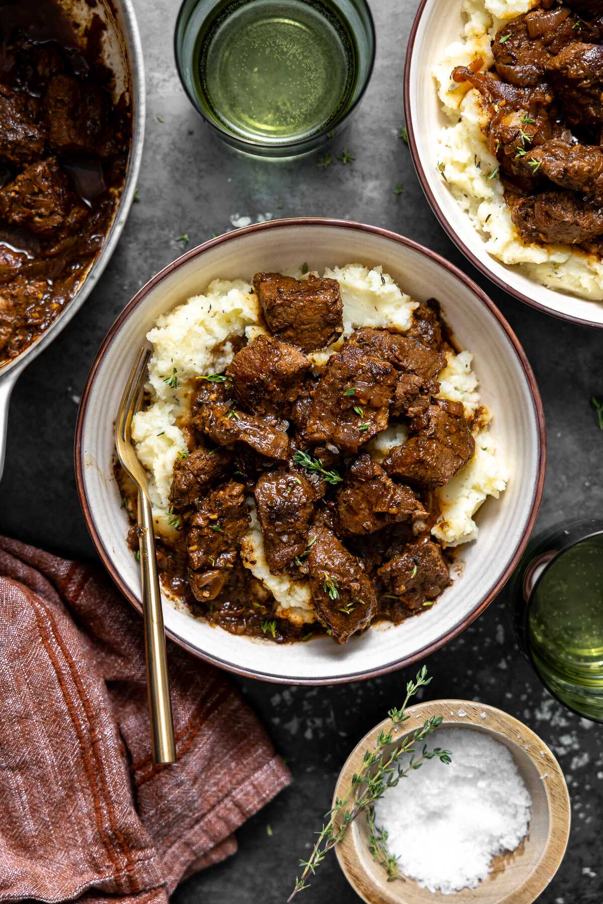 French onion braised beef tips served over mashed potatoes with a gold spoon 
