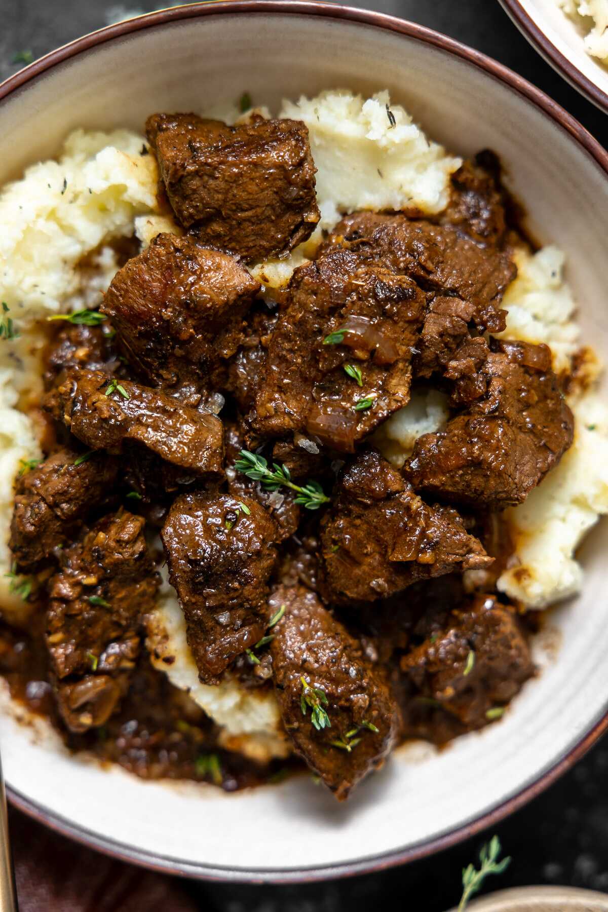 a close up picture of french onion braised beef tips sereved over mashed potatoes 