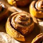 A pan of glazed pumpkin spice latte cinnamon rolls sitting in sunlight.