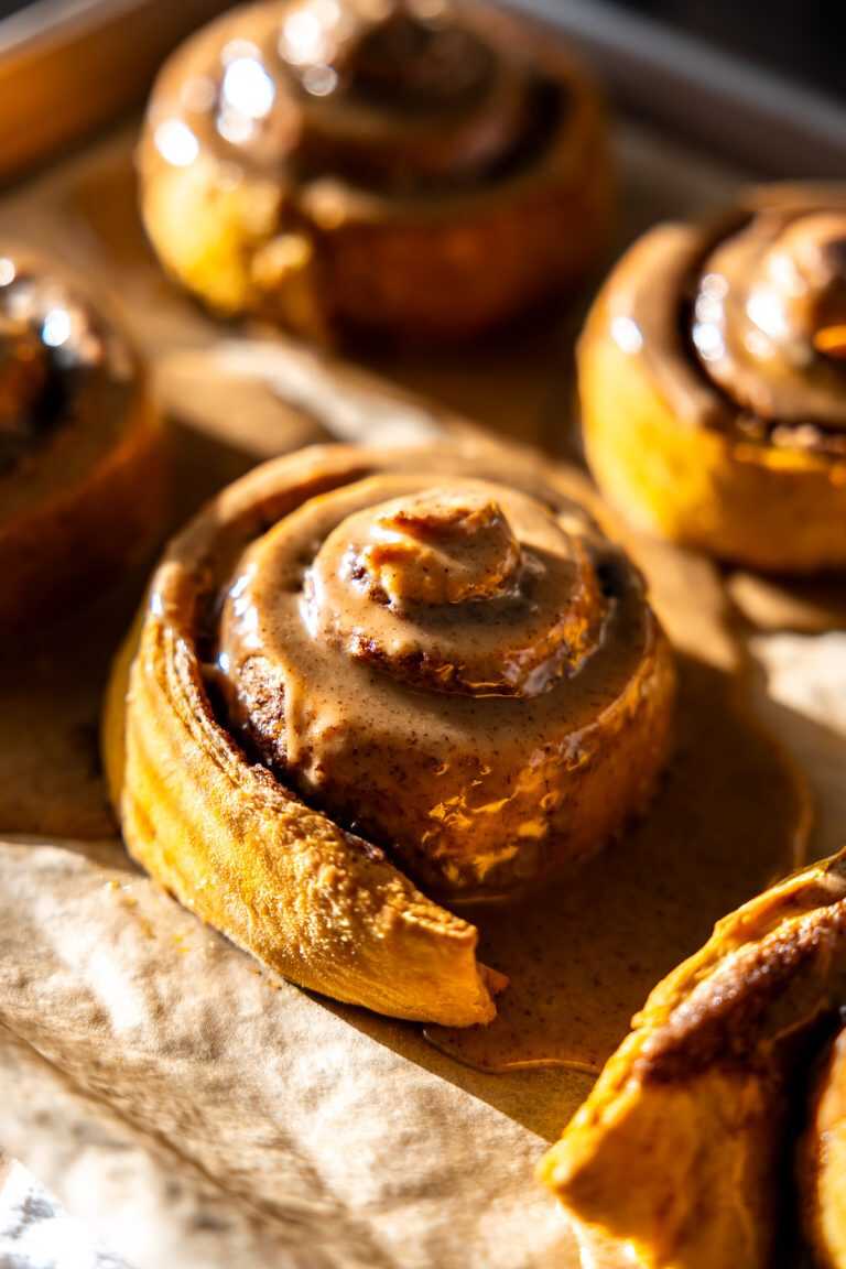A pan of glazed pumpkin spice latte cinnamon rolls sitting in sunlight.