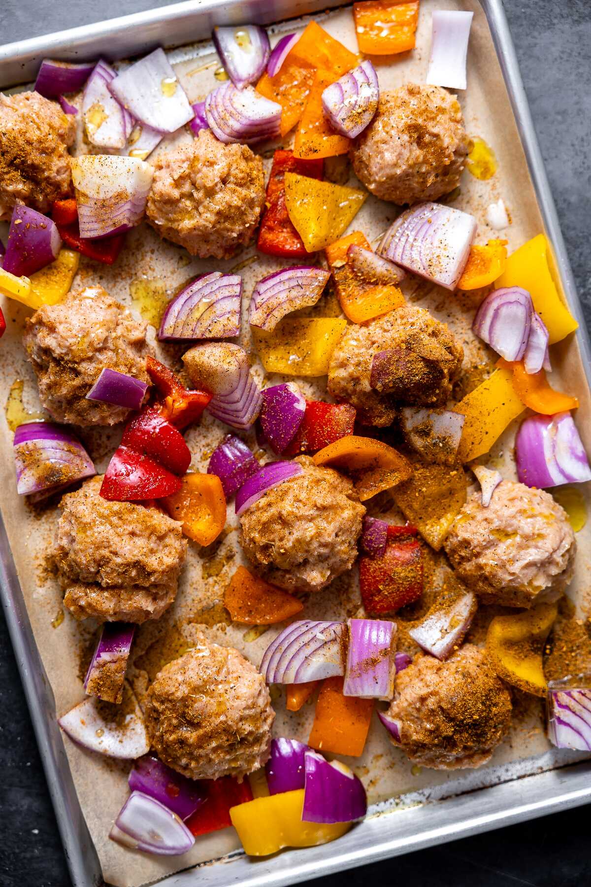 Cajun chicken meatballs and vegetables on a sheet pan prior to baking. 