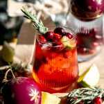 A mistletoe margarita topped with cranberries, lime wedges and a sugared rosemary sprig.