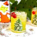The Grinch cocktail in a Christmas glass with the Grinch in the background.