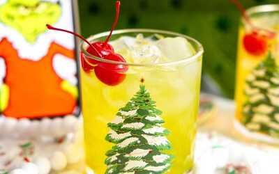 The Grinch cocktail in a Christmas glass with the Grinch in the background.