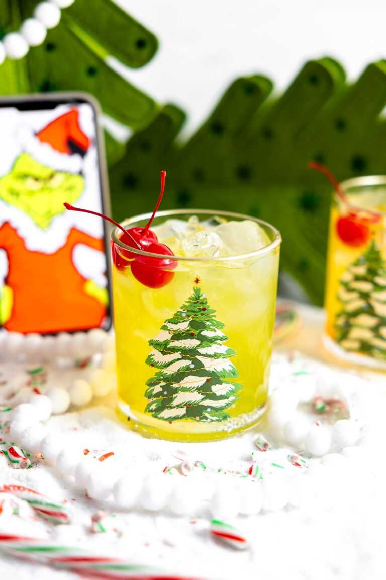 The Grinch cocktail in a Christmas glass with the Grinch in the background.