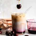 A cherry being dropped into an cherry vanilla iced latte.