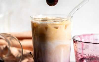 A cherry being dropped into an cherry vanilla iced latte.