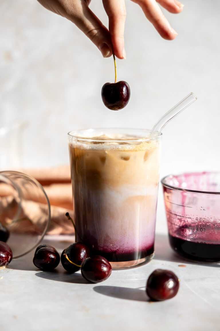 A cherry being dropped into an cherry vanilla iced latte.